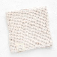 Powder: A folded waffle-weave linen washcloth in cream color with a logo patch.