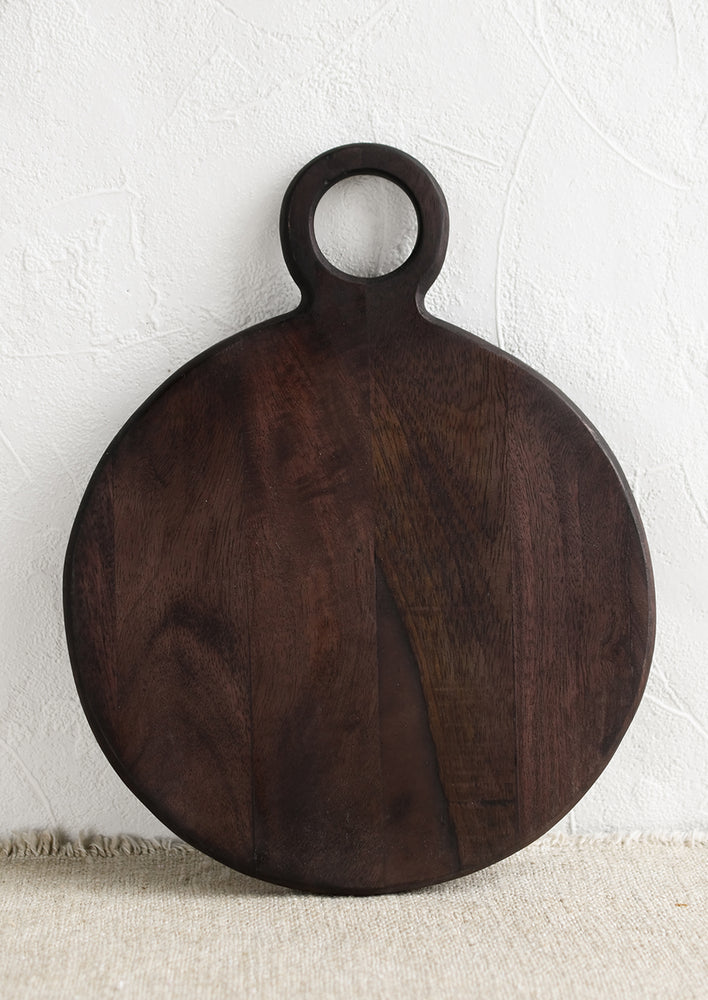 A dark wash wood cutting board with circular shape and cutout circle handle.