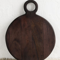 1: A dark wash wood cutting board with circular shape and cutout circle handle.