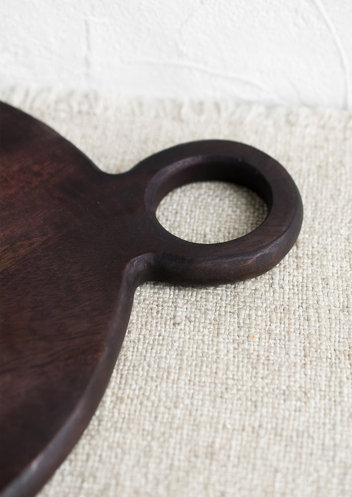 2: A dark wash wood cutting board with circular shape and cutout circle handle.