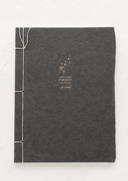 A journal with dark grey cover with Walt Whitman quote.