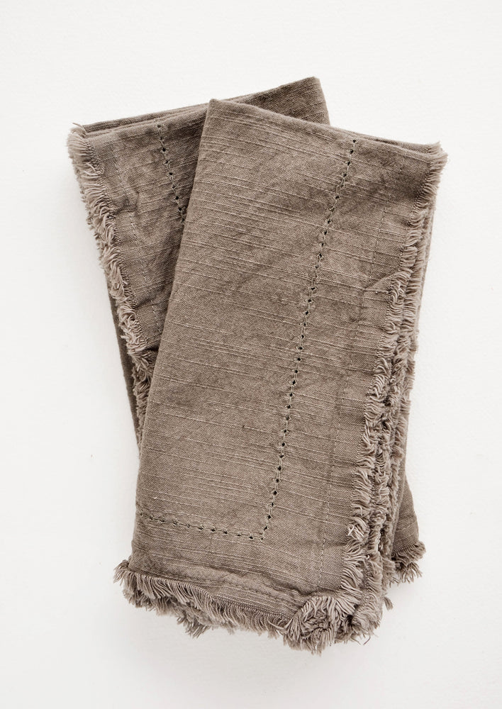 Two folded brown Cotton Napkins with frayed edges .
