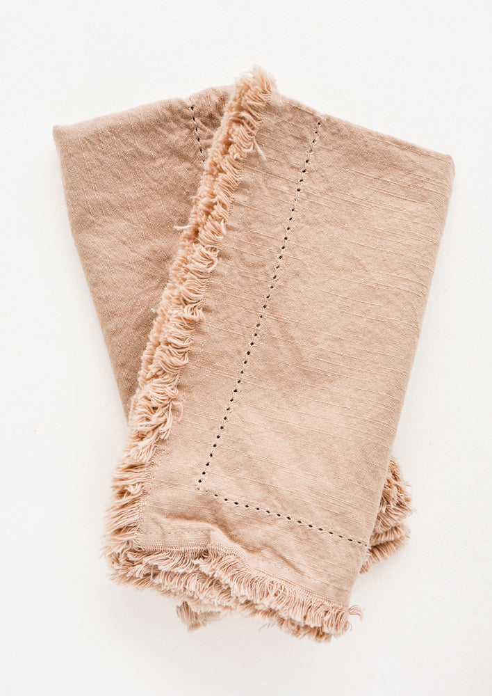 Cocoa: Two folded tan Cotton Napkins with frayed edges .