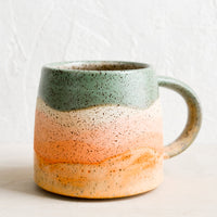 Coral Multi: A ceramic mug with handle in wavy stripe design in celadon, coral and orange.
