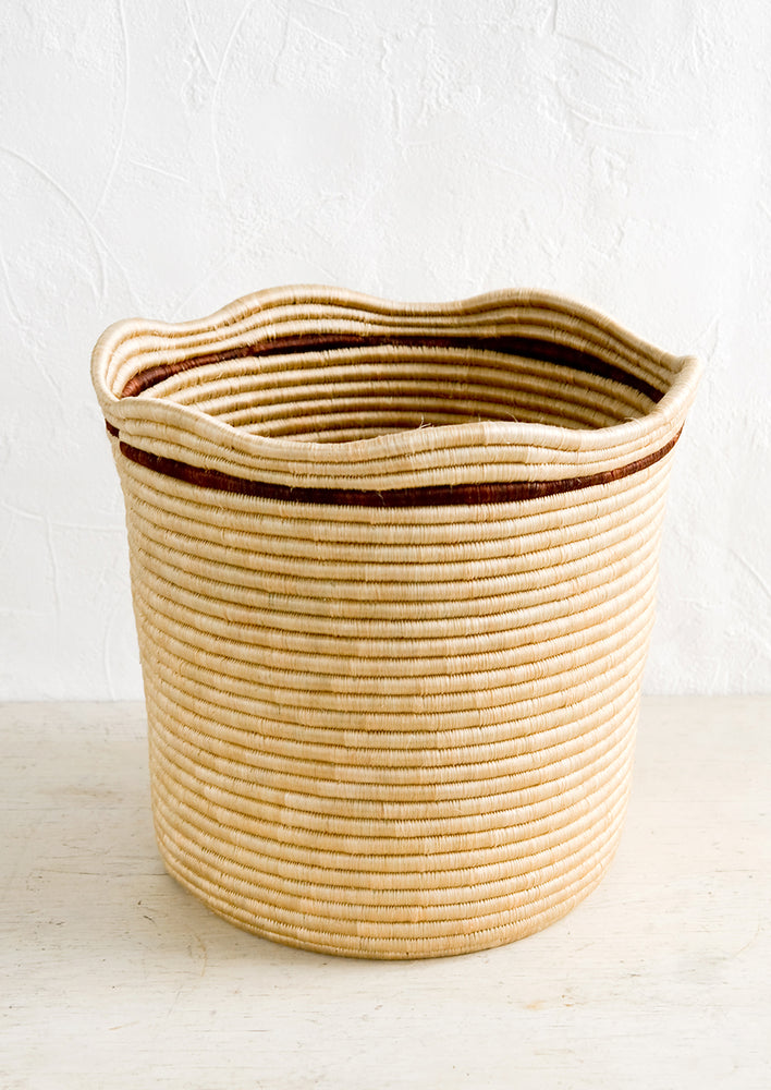 Beige Multi: A woven sweetgrass storage bin in natural color with a wavy top rim and contrast stripe detail around rim.