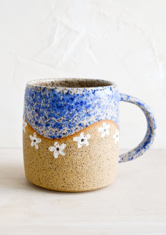A speckled ceramic coffee mug in blue with wavy line of ivory daisies at middle.