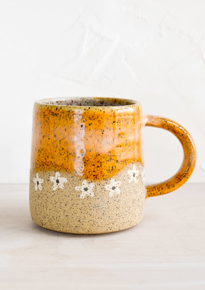 A speckled ceramic coffee mug in caramel with wavy line of ivory daisies at middle.