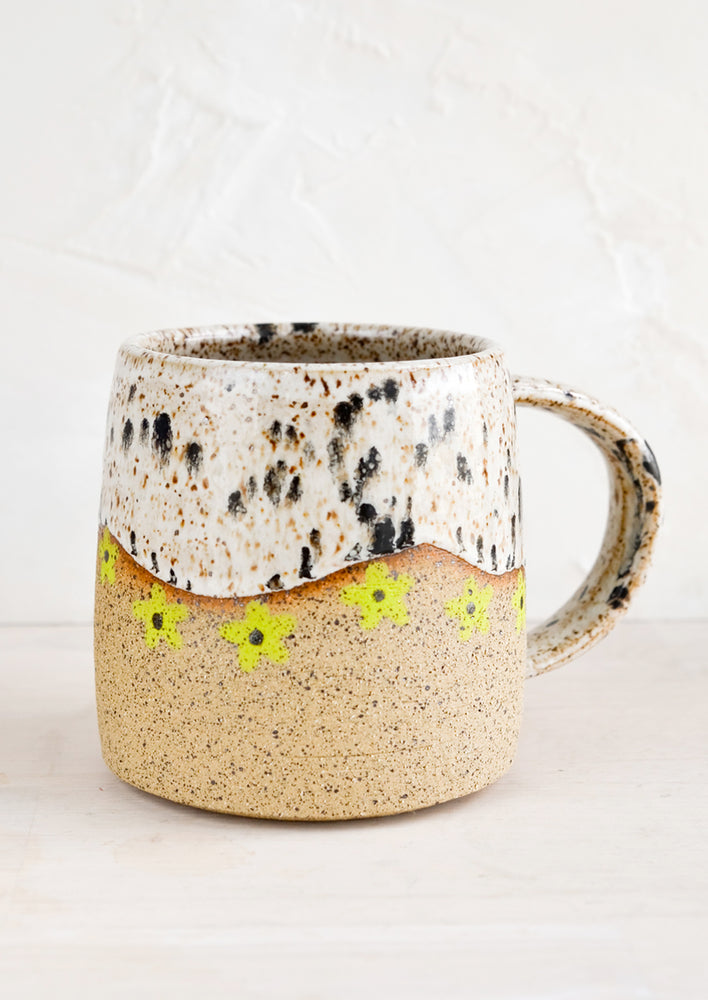 Appaloosa / Lime: A speckled ceramic coffee mug in black and white with wavy line of lime green daisies at middle.