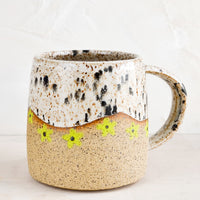 Appaloosa / Lime: A speckled ceramic coffee mug in black and white with wavy line of lime green daisies at middle.
