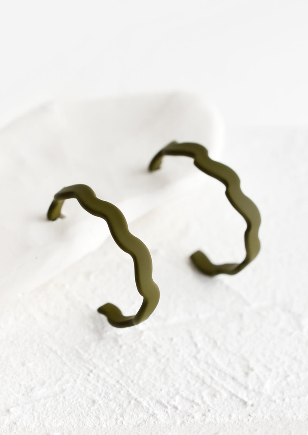 Army: A pair of hoop earrings in matte olive with wavy shape.