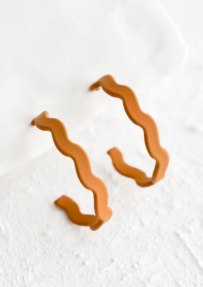 Caramel: A pair of hoop earrings in matte caramel with wavy shape.