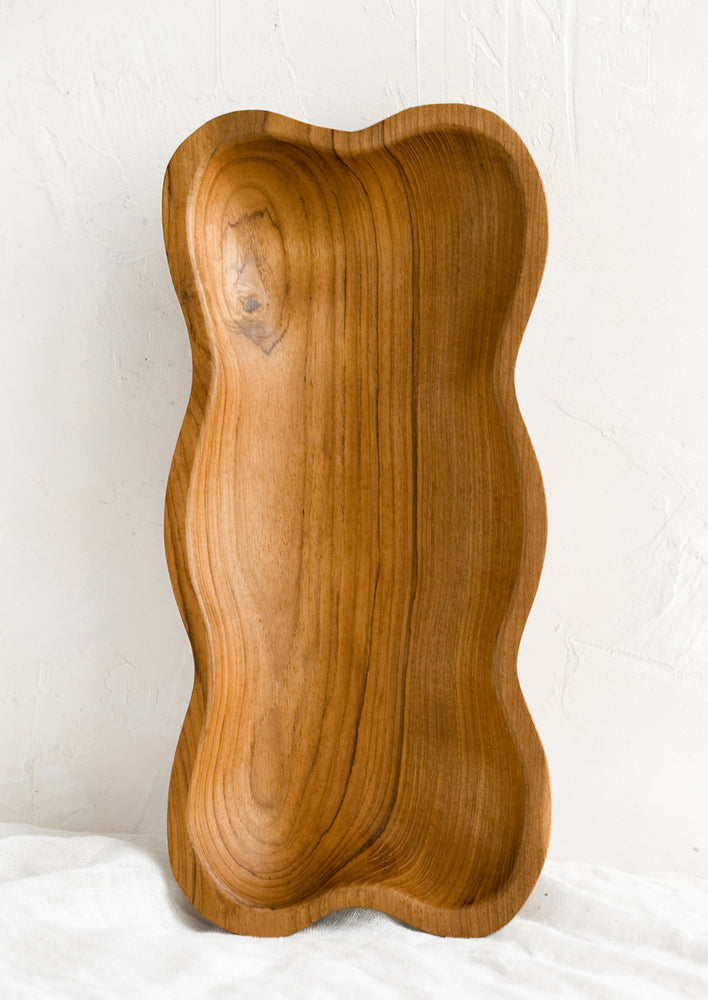 A rectangular teakwood shallow bowl with wavy shape.