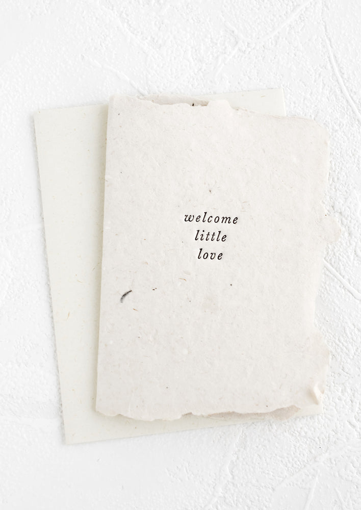 A greeting card made from natural handmade paper and small lowercase text on front reading "Welcome little love".