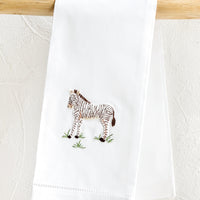 Zebra: A white folded cotton hand towel with embroidered zebra design.