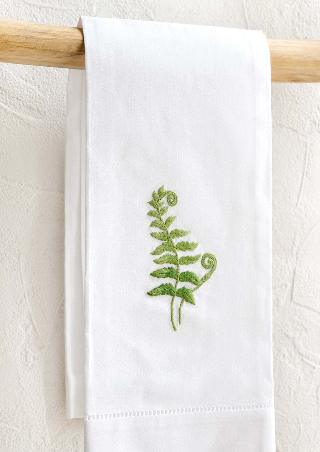 Fern Frond: A white folded cotton hand towel with embroidered fern design.
