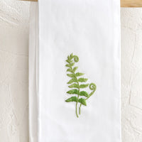 Fern Frond: A white folded cotton hand towel with embroidered fern design.