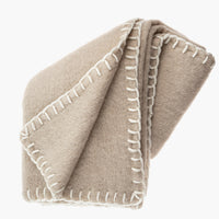 Oat: A beige mohair blanket with white yarn whipstitched trim.