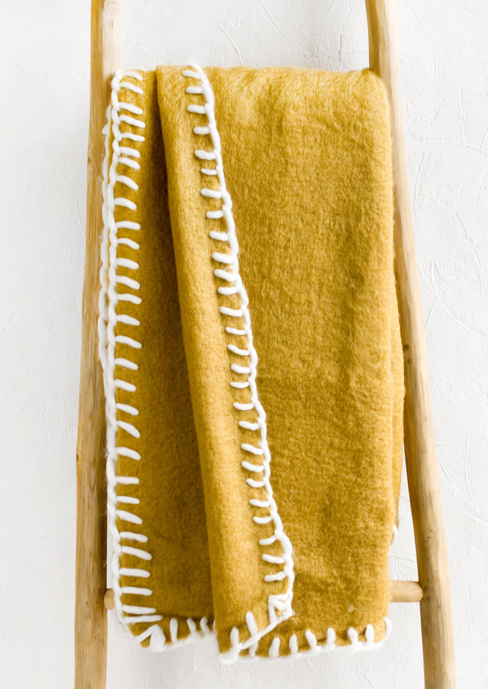 A mustard mohair blanket with white yarn whipstitched trim.