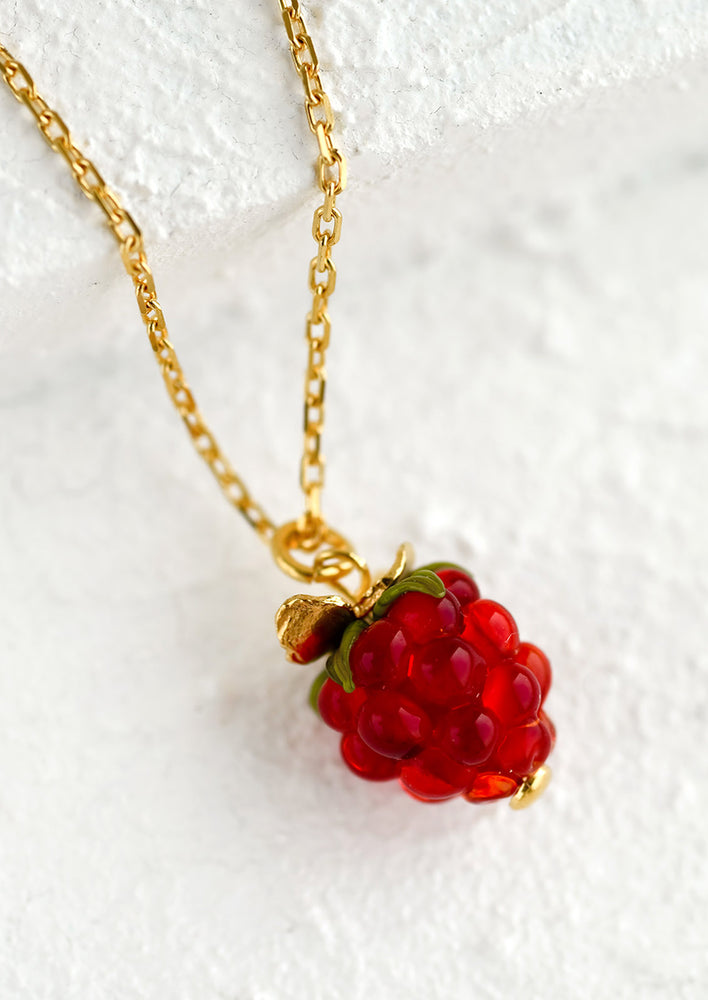 A gold necklace with glass raspberry charm.