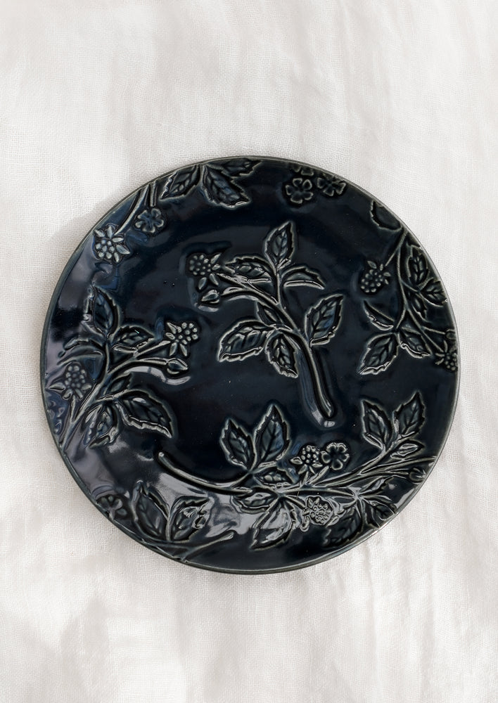 A round ceramic dessert plate in indigo with tonal raspberry pattern.