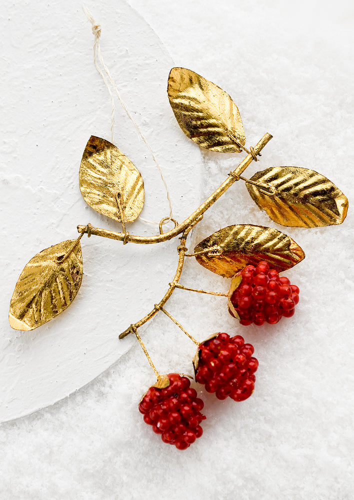 A holiday ornament with red berries on gold leafy branch.