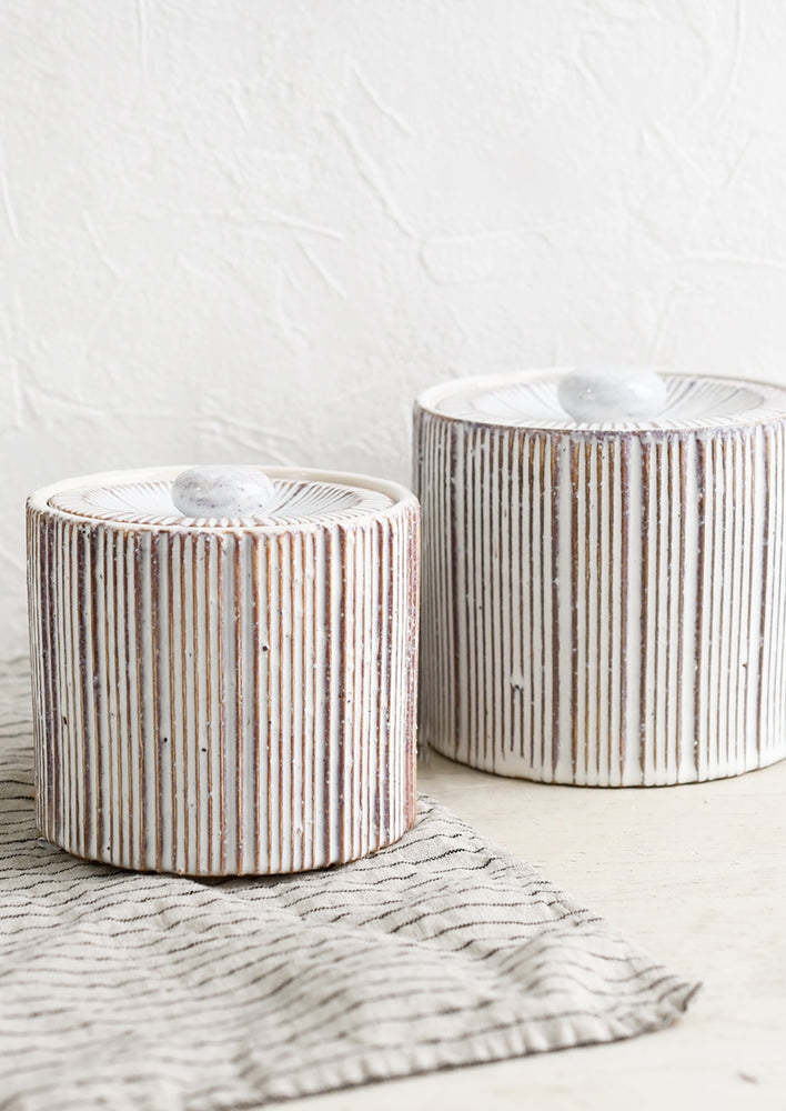 Two cylindrical lidded ceramic jars in white with contrasting ribbed texture.