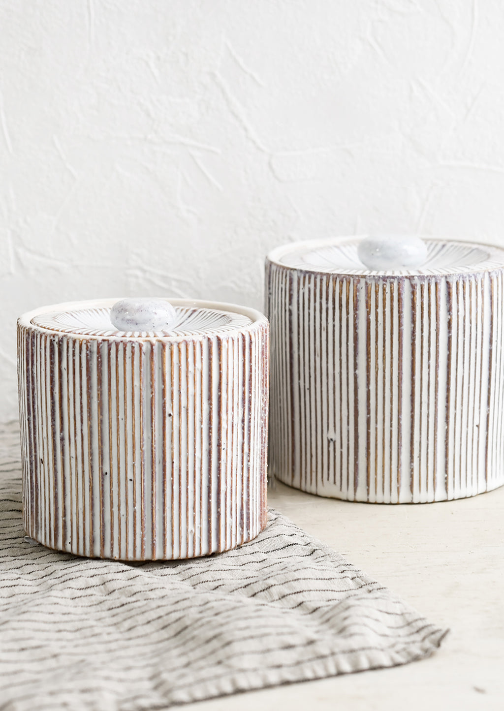 2: Two cylindrical lidded ceramic jars in white with contrasting ribbed texture.