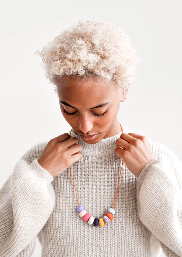 Model wears sweater and necklace with nine clay beads. 