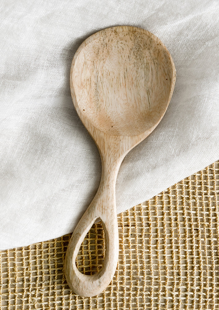 A wide paddle shaped spoon in light colored wood with loop handle.
