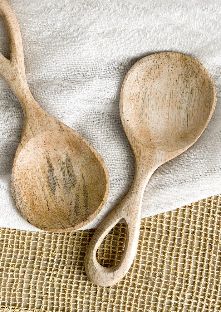 A wide paddle shaped spoon in light colored wood with loop handle.