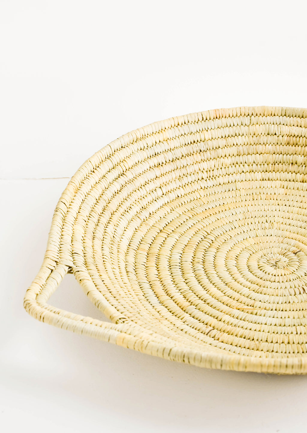 2: Flat, round platter woven from natural straw with handles at sides