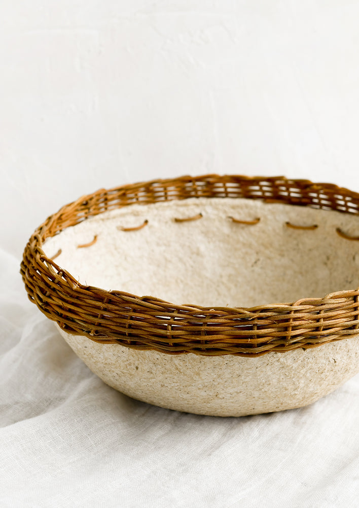 A natural paper mache bowl with brown wicker trim at top.
