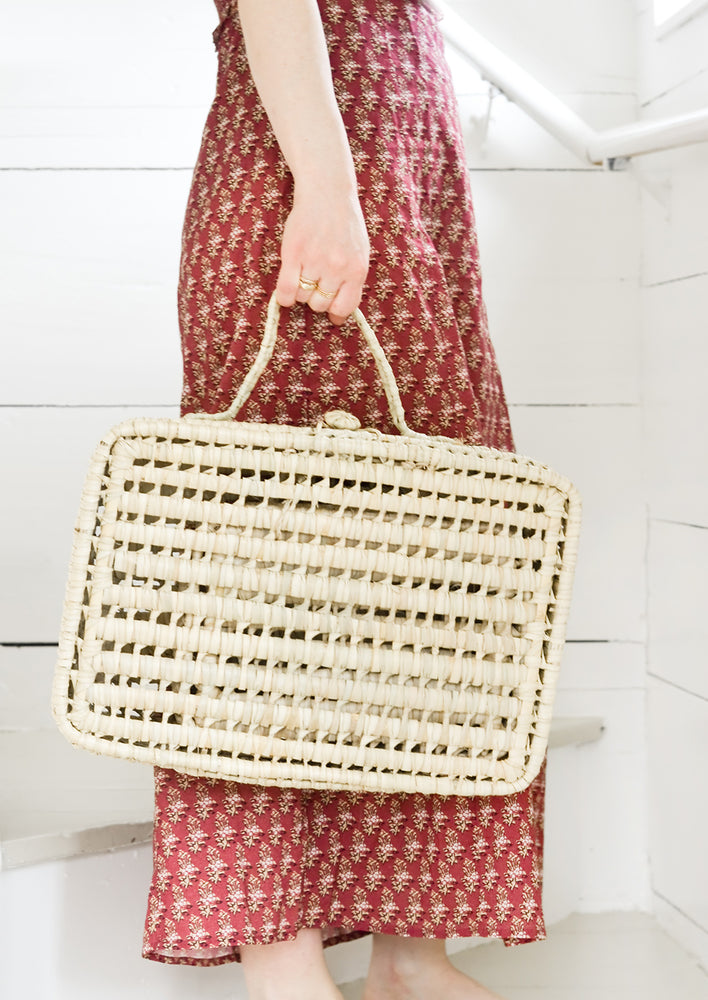 A women holding a woven suitcase.