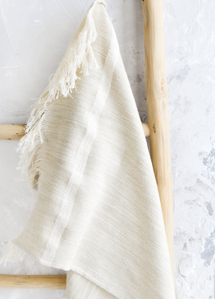 A woven kitchen towel in white hanging on a ladder.