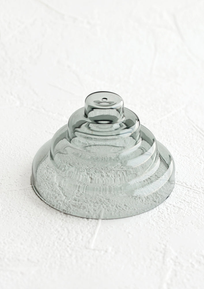 An incense holder made of glass in sculptural design with small hole at top, in grey.