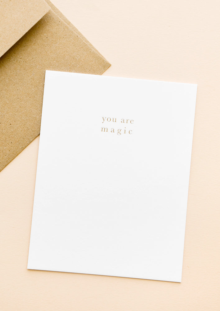 A brown paper envelope and white greeting card with the words "you are magic" in small gold text.