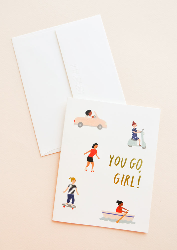 A white envelope and a greeting card with little illustrations of women in motion and the words "you go girl" in gold foil.