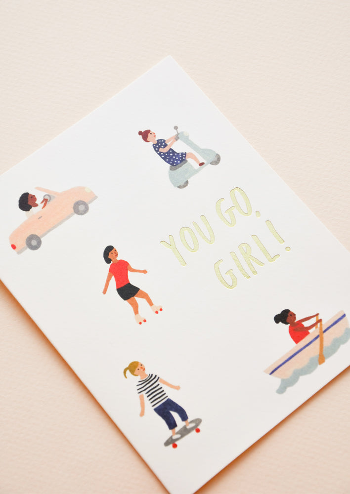 A greeting card with little illustrations of women in motion and the words "you go girl" in gold foil.