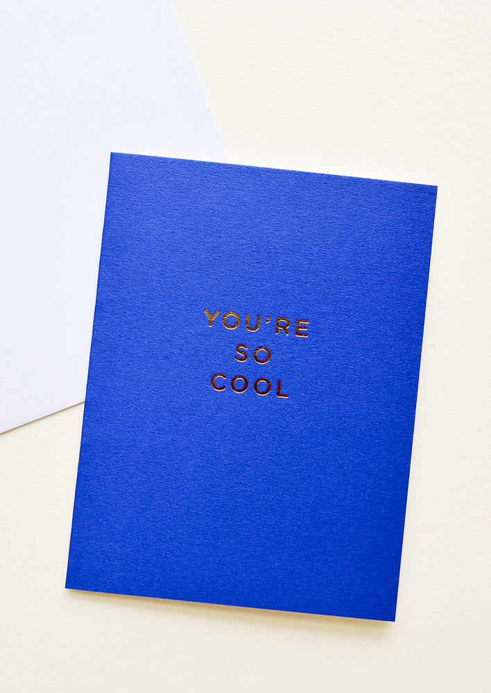 1: Notecard with gold foil text "You're so cool" on bright cobalt background, with white envelope.
