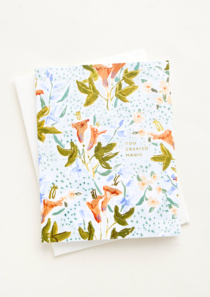 1: Greeting card with floral illustrated background and small gold lettering reading "You Created Magic"