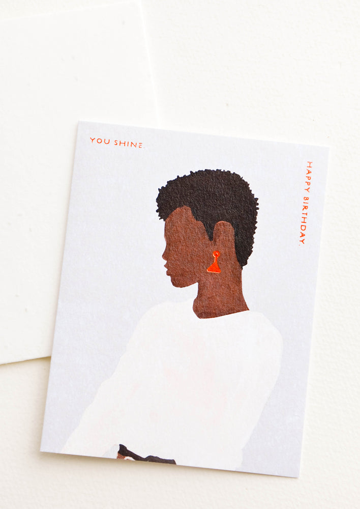 Greeting card with silhouetted profile of a woman wearing earrings, copper text reads "You Shine. Happy Birthday"