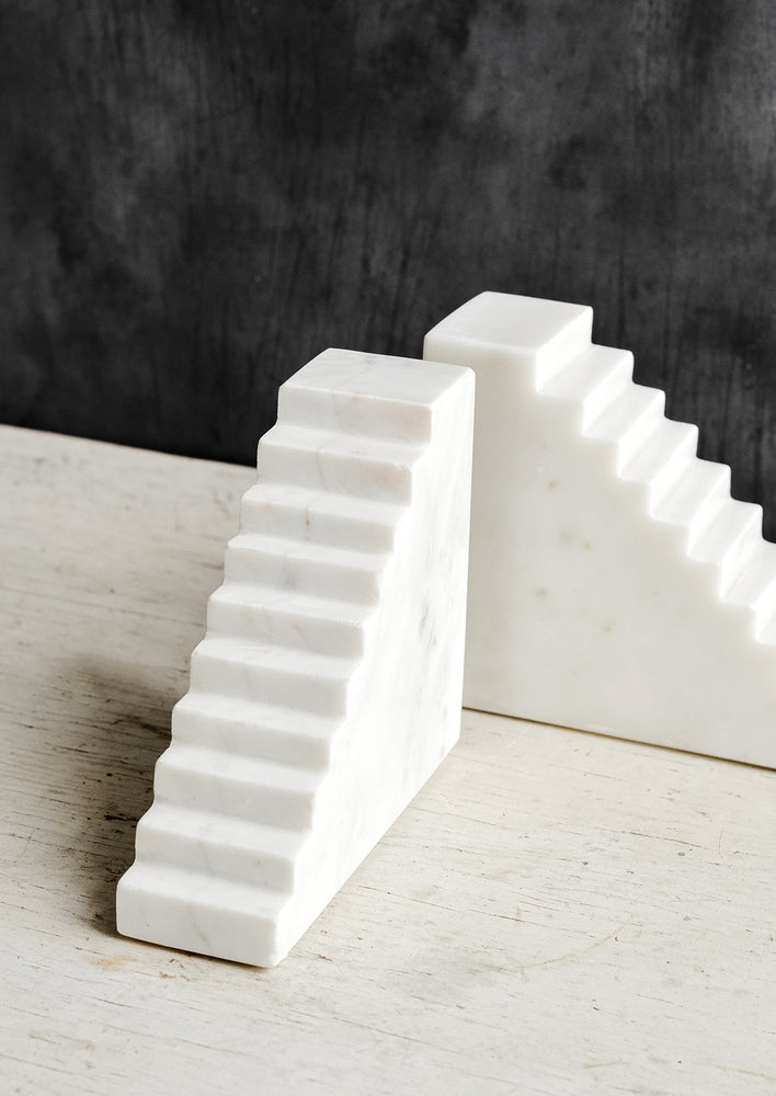 A pair of white marble bookends with staircase design.