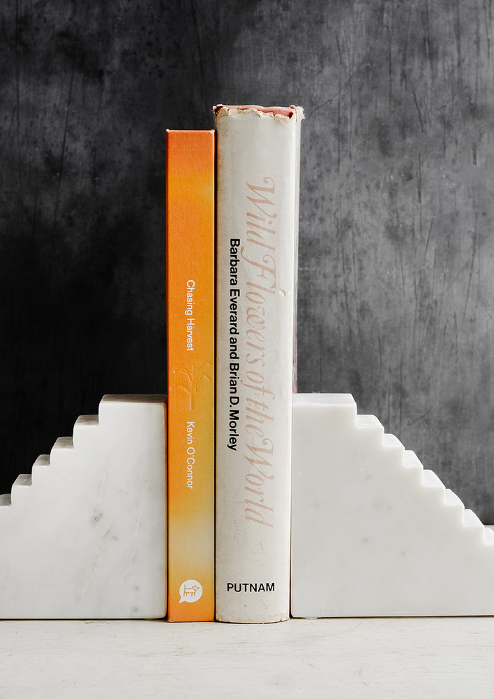 A pair of white marble bookends with staircase design, shown with two books.