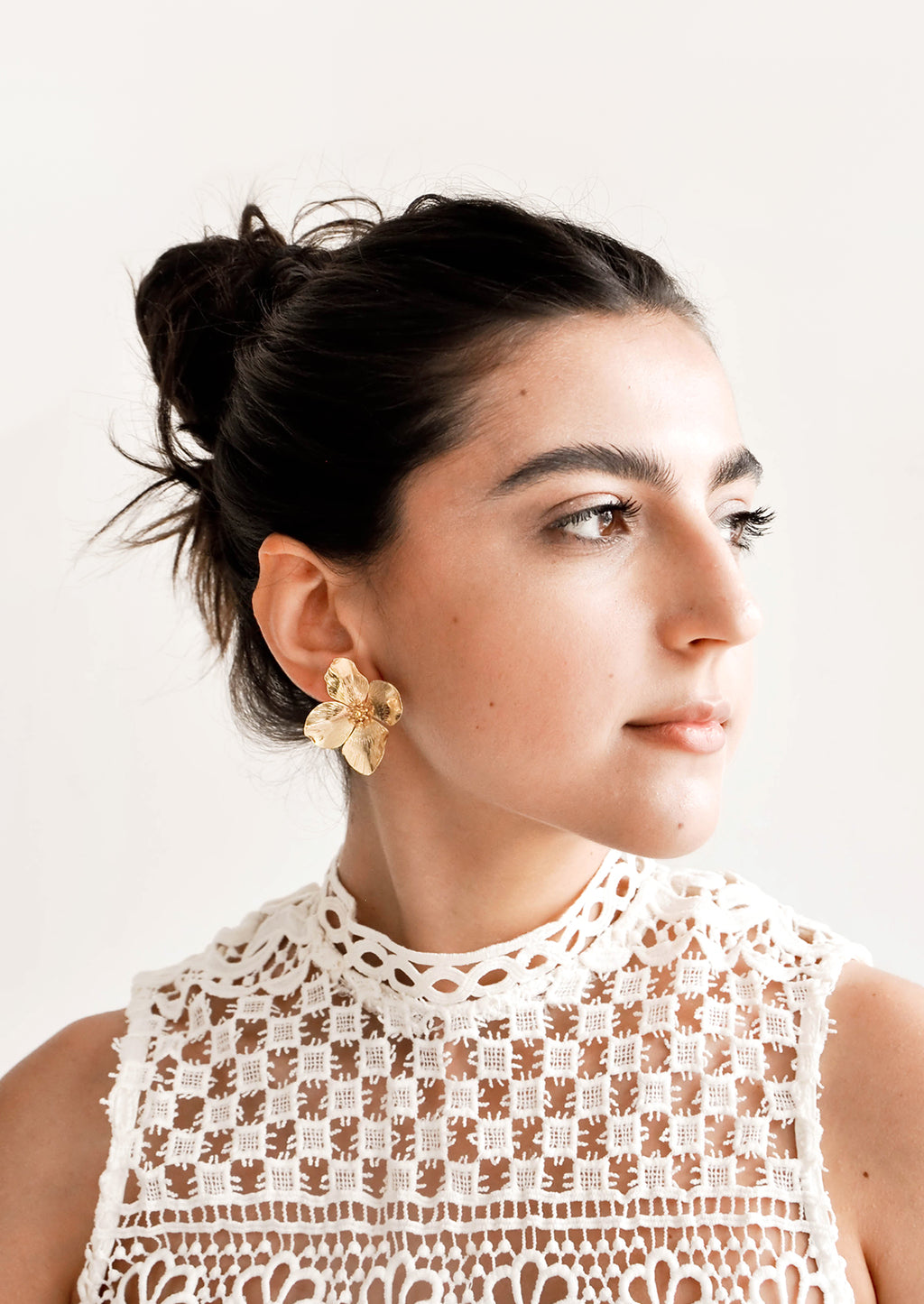 2: Model wears gold flower-shaped earrings and white top.