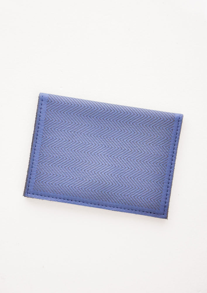 Indigo Blue: Slim dark blue leather wallet with two interior slip pockets that folds closed with a snap, shown closed with zig zag etched pattern. 