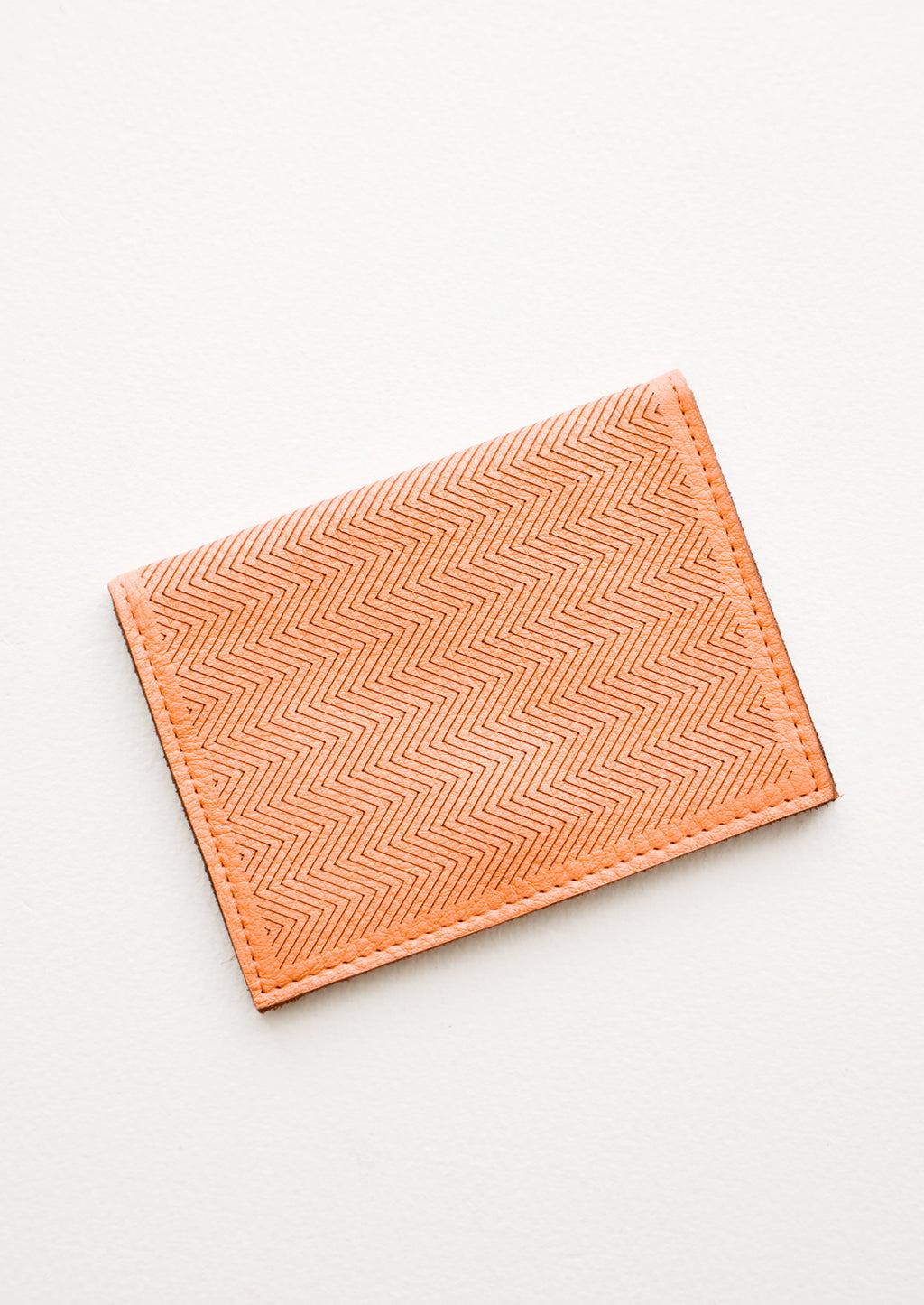 Terracotta: Slim terracotta orange leather wallet with two interior slip pockets that folds closed with a snap, shown closed with zig zag etched pattern. 