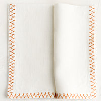 Orange Zest: A white linen napkin with orange embroidered zig zag border.