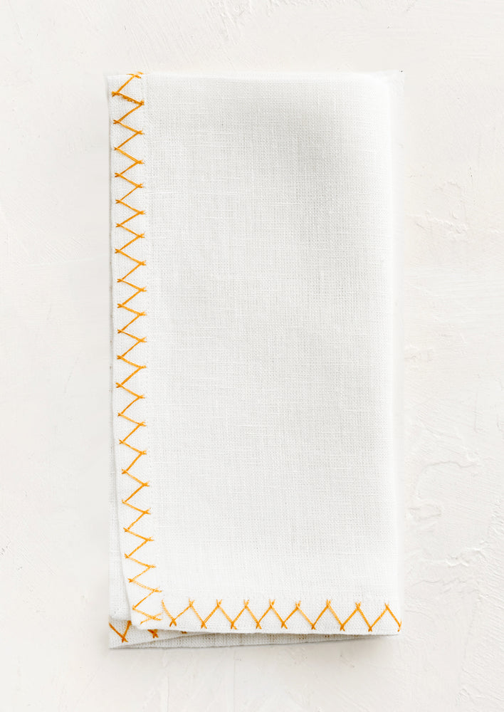Mustard: A white linen napkin with yellow embroidered zig zag border.